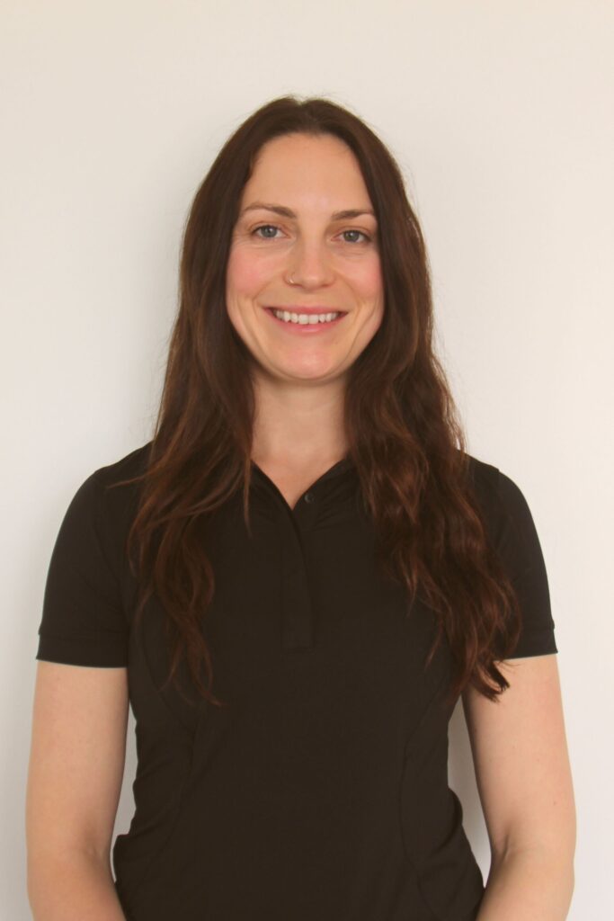 A smiling woman with long, dark hair is wearing a black polo shirt, standing against a plain white background. The image is associated with Friday Health.