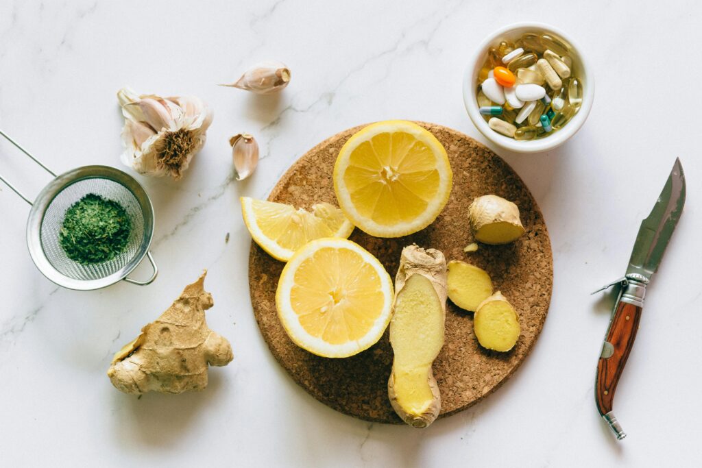 Alt text: A cork board displays fresh ingredients for wellness, including sliced lemons, ginger root, garlic cloves, and a small bowl of assorted vitamins and supplements, emphasizing a focus on Friday Health.