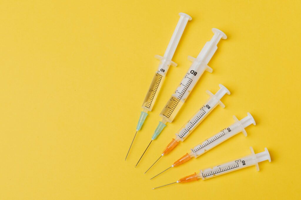 Alt text: A collection of syringes with varying amounts of liquid, arranged on a bright yellow background, representing Friday Health's focus on health and wellness.