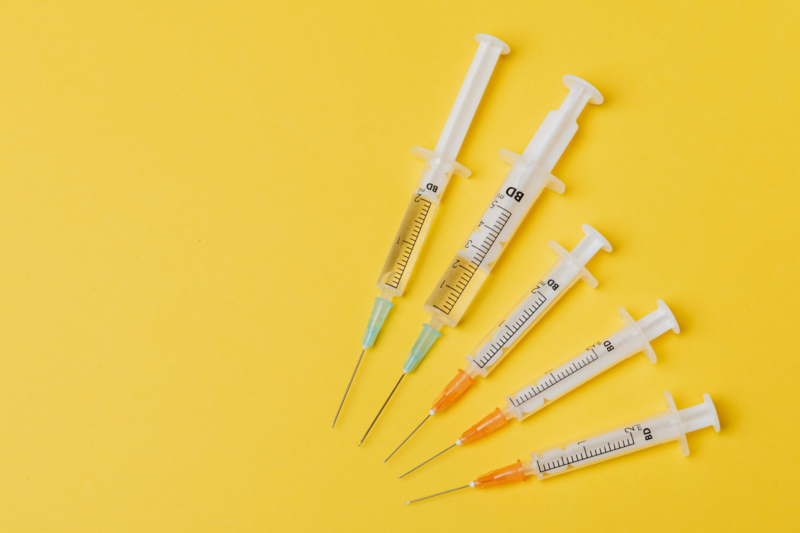Alt text: A collection of syringes with varying amounts of liquid, arranged on a bright yellow background, representing Friday Health's focus on health and wellness.
