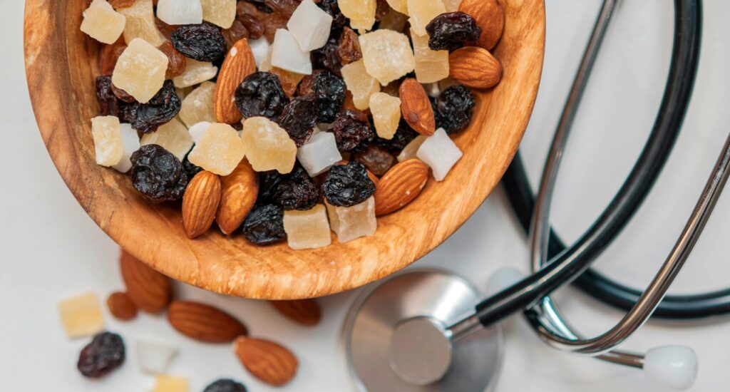 A wooden bowl filled with a variety of nuts and dried fruits, including raisins, almonds, and candied pieces, alongside a stethoscope, representing a theme of health and wellness associated with Friday Health.