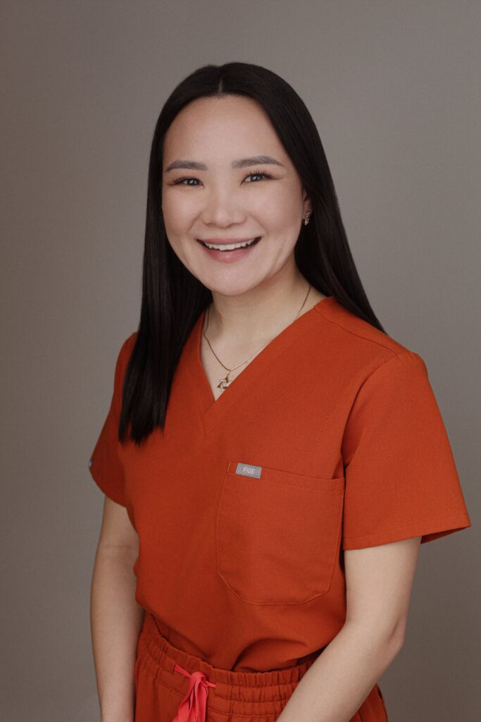 A smiling medical professional in an orange scrub top poses against a neutral background, representing Friday Health.