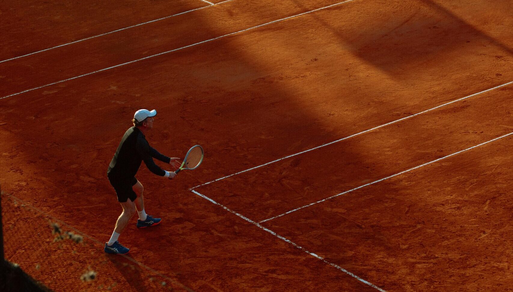 High-angle view of an active tennis game on a clay court during sunset, capturing dynamic play.
