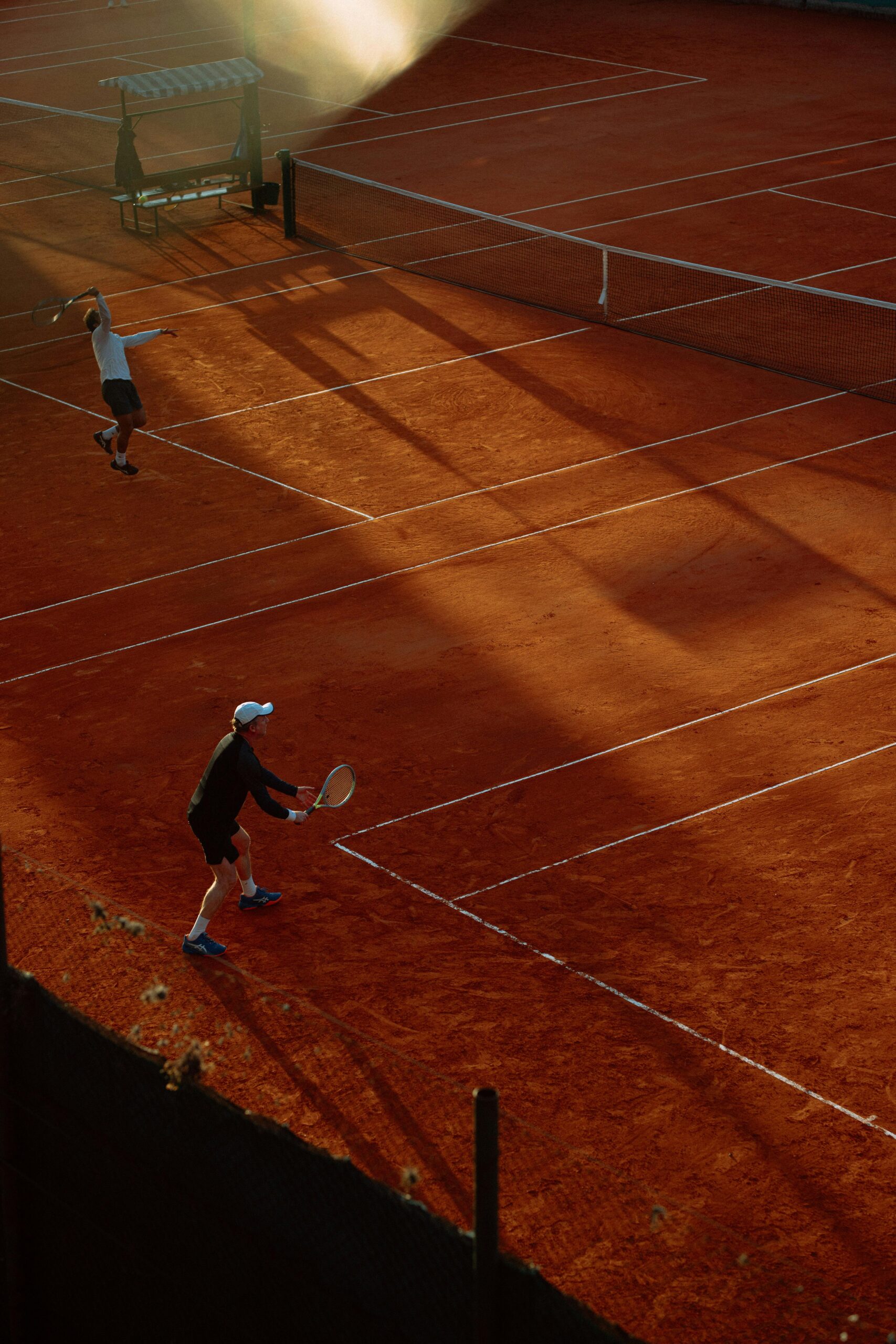 High-angle view of an active tennis game on a clay court during sunset, capturing dynamic play.