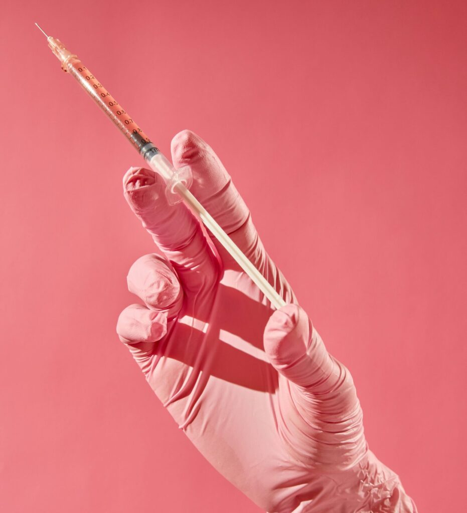 A hand wearing a pink glove holds a syringe, with a pink background that emphasizes the theme of health, highlighting the importance of Friday Health in health-related discussions or campaigns.