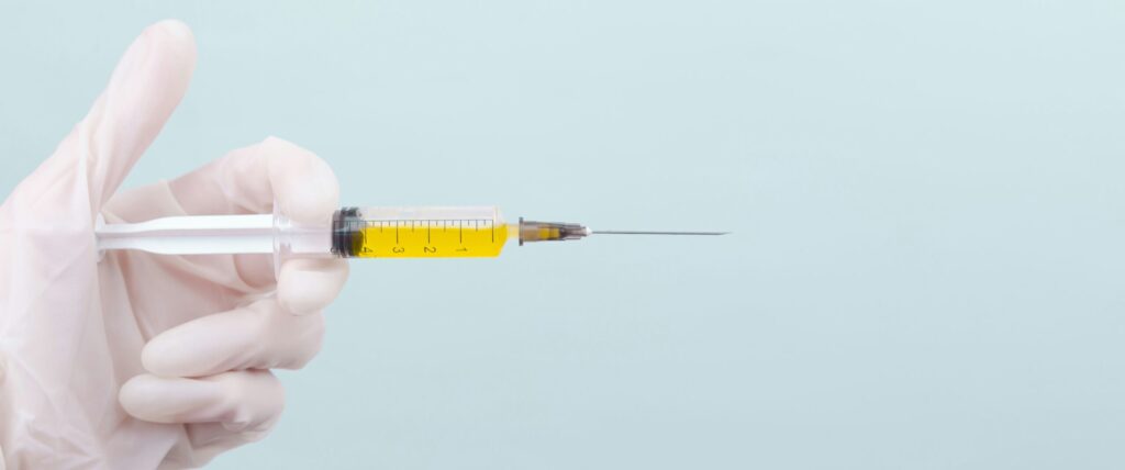 A close-up image of a hand in a glove holding a syringe filled with yellow liquid, representing a concept related to Friday Health.