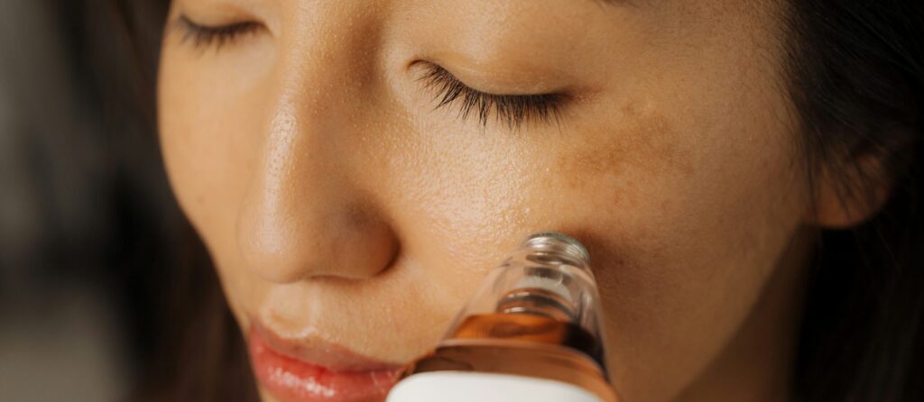 A woman is seen closely, eyes closed, using a facial treatment device on her cheek. The image emphasizes skincare, showcasing the woman's smooth skin and the device's application, representing a focus on beauty and wellness channels such as Friday Health.