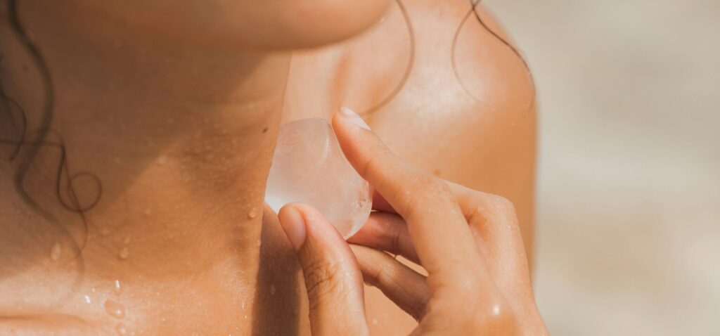 A close-up image of a person's neck where they are applying a piece of ice to their skin, with droplets of water visible. The image conveys a sense of refreshing self-care, highlighting the concept of wellness associated with Friday Health.