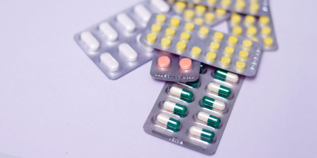 Alt text: A collection of medication blisters, including white, yellow, pink, and green capsules, indicating a focus on Friday Health products.