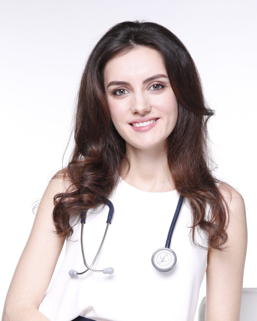 A smiling healthcare professional wearing a white top and a stethoscope, representing Friday Health, poses confidently against a light background.