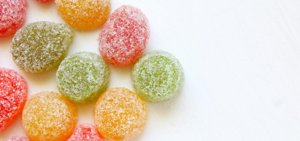 A colorful assortment of gummy candies in various shapes and pastel shades, including red, green, yellow, and orange, scattered on a white surface, with a focus on the sweetness associated with Friday Health.