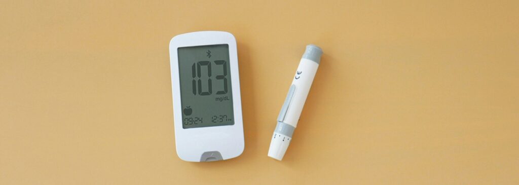A digital glucose meter displaying a reading of 103 mg/dL alongside an injection pen, both set against a light orange background, representing Friday Health.