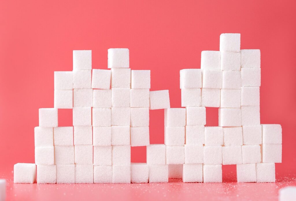 Alt text: A creative arrangement of sugar cubes stacked in different formations on a pink background, symbolizing sweetness and health, related to Friday Health.
