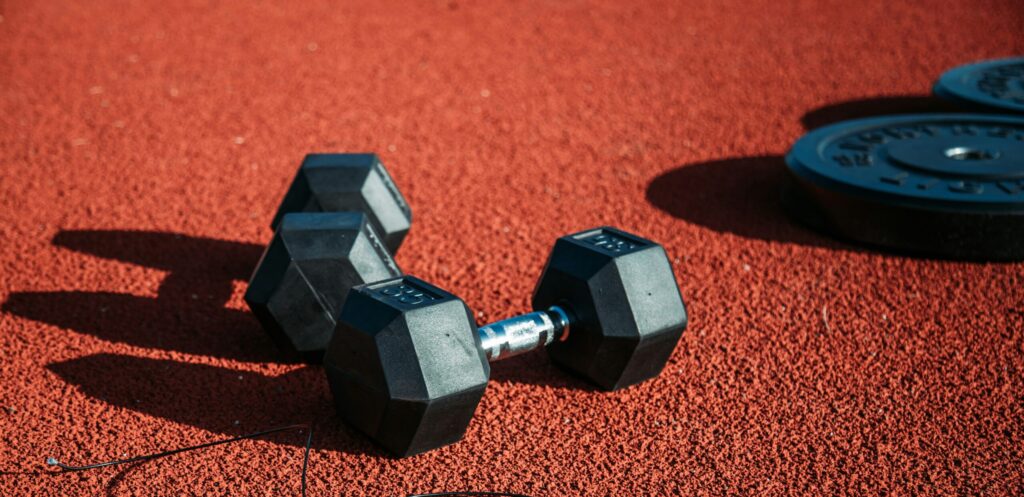 Alt text: A pair of black dumbbells rests on a red rubber surface, with a skipping rope tangled nearby, representing the theme of Friday Health and fitness activities.