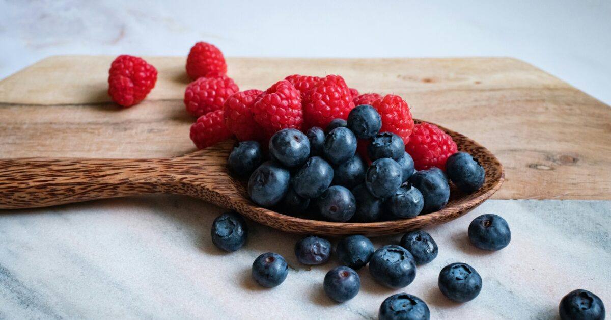 A wooden spoon holds an assortment of fresh blueberries and raspberries, placed on a light-colored marble surface, reflecting the vibrant colors of Friday Health by promoting healthy eating.