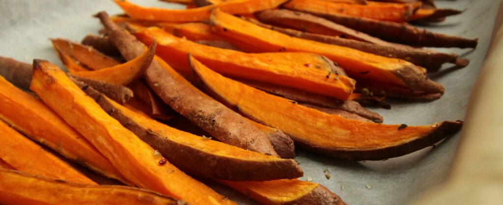 Baked sweet potato fries arranged on parchment paper, showcasing a vibrant orange color, promoting Friday Health's commitment to healthy eating options.