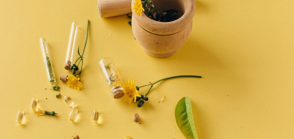 Natural herbal supplements and remedies displayed with a mortar and pestle on a vibrant yellow surface.