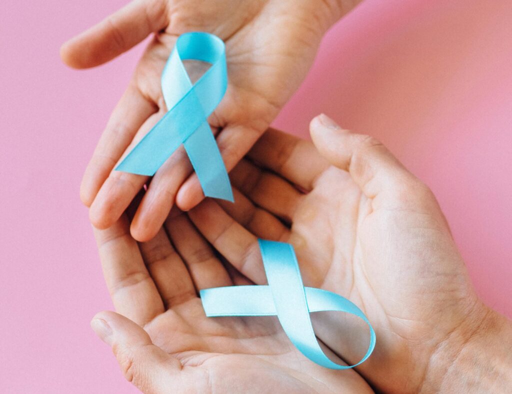 Two hands holding blue awareness ribbons on a pink background, symbolizing support and awareness.